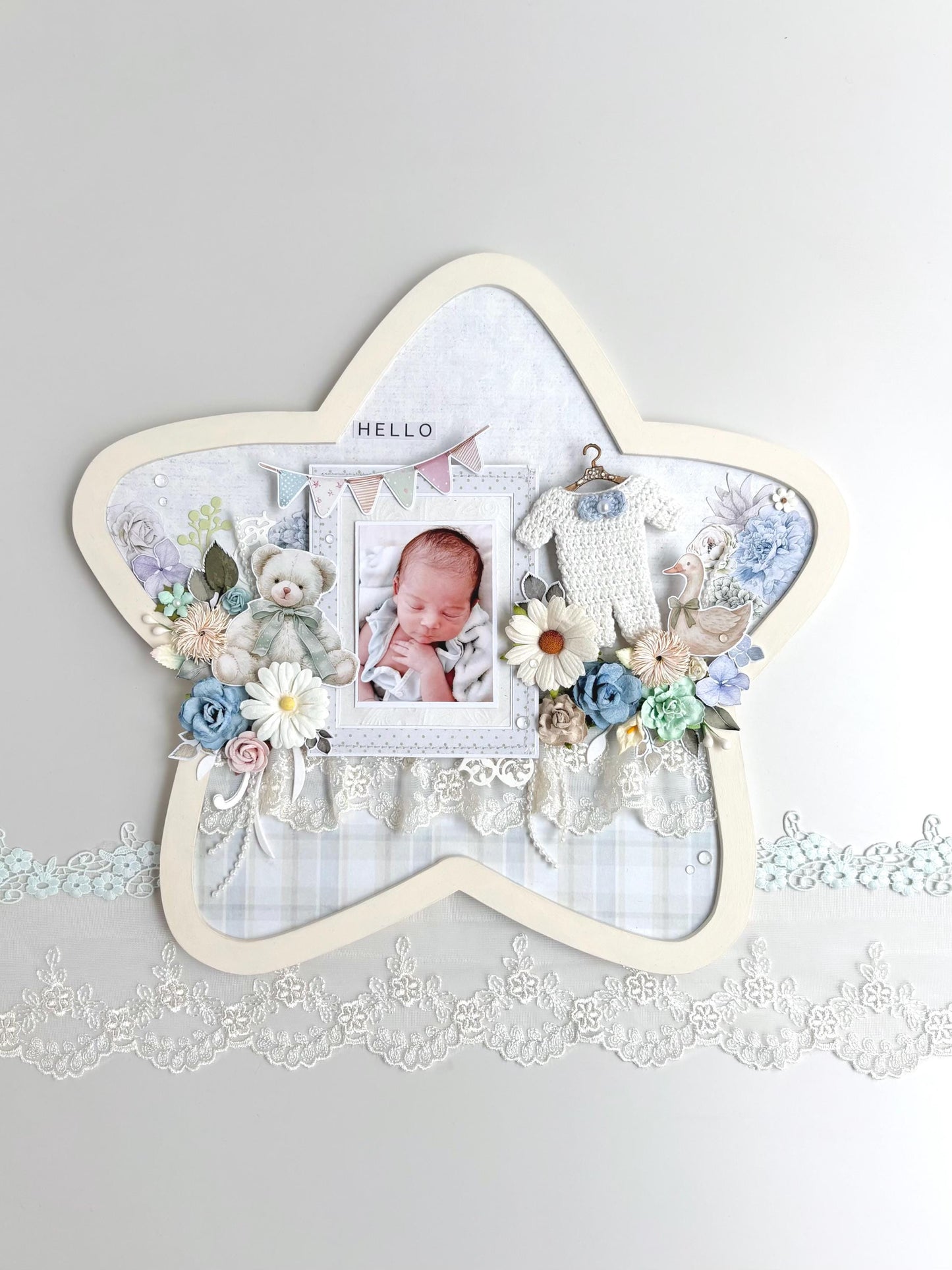 Star-shaped nursery keepsake frame with a baby photo, teddy bear, pastel florals, a tiny crocheted onesie, and a Hello banner