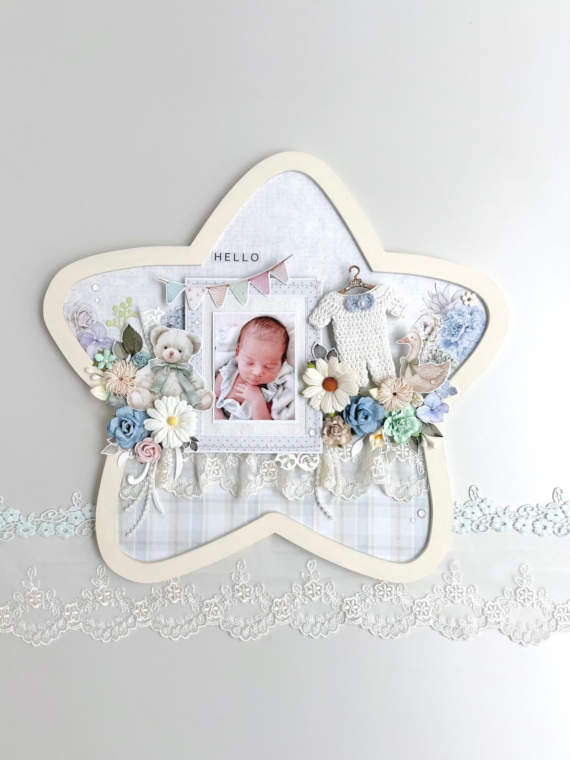 Star-shaped nursery keepsake frame with a baby photo, teddy bear, pastel florals, a tiny crocheted onesie, and a Hello banner