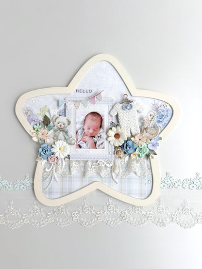 Star-shaped nursery keepsake frame with a baby photo, teddy bear, pastel florals, a tiny crocheted onesie, and a Hello banner